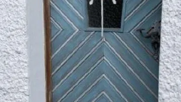 Rustikale Eingangstür in Blau mit dekorativem Gitter und weißer Putzfassade.