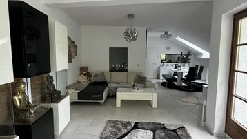 Helles, offenes Wohnzimmer mit modernen Möbeln, Fliesenboden und Blick in den Essbereich.