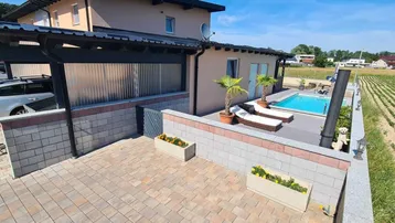 Ansicht des Hauses mit Carport, Poolbereich und Liegestühlen, umgeben von Feldern.