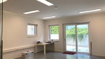 Modernes Büro mit großen Schiebetüren zur Terrasse und viel Tageslicht, ausgestattet mit Einbaulampen.
