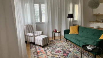 Helles Wohn- und Esszimmer mit gemütlichem Sofa, Sessel und integrierter Küchenzeile.