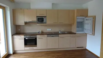 Moderne Einbauküche mit hellen Holzfronten, integrierten Geräten und Laminatboden.