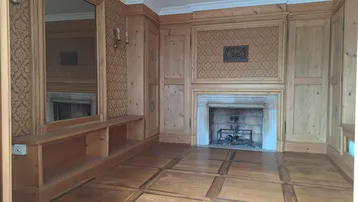 Traditionelles Zimmer mit Holztäfelung, Kamin und gemusterten Tapeten in warmen Farbtönen.