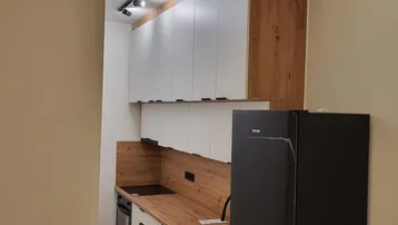 Moderne Küche mit weißen Schränken, Holzoptik-Arbeitsplatte und schwarzem Kühlschrank.