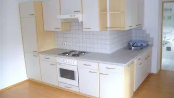 Funktionale Küche mit weißen Schränken, hellen Holzdetails, Herd und Spüle, ideal für den täglichen Gebrauch.