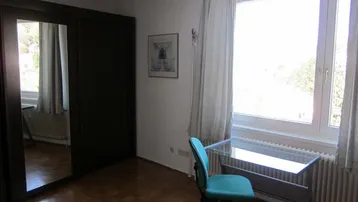 Helles Schlafzimmer mit großem Fenster, Spiegelschrank und Parkettboden, ideal als Arbeits- und Schlafbereich.