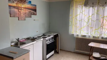 Kleine Küche mit Herd, Spüle und Fenster, ausgestattet mit einfachen Geräten und hellblauen Wänden.