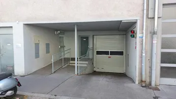 Eingangsbereich einer Tiefgarage mit Rampe und Rolltor, daneben ein Gehweg.