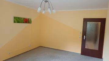 Heller Raum mit gelb gestrichenen Wänden, Teppichboden und einer Deckenleuchte.