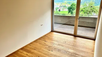 Heller Raum mit Holzboden, großen Fenstern und Zugang zu einem Balkon mit Bergblick.
