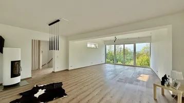 Helles und geräumiges Wohnzimmer mit modernem Kamin, Holzboden und großen Fenstern.