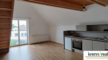 Heller Wohnbereich in einem Dachgeschoss-Apartment mit Holzbalken, Parkettboden und Zugang zu einem kleinen Balkon.