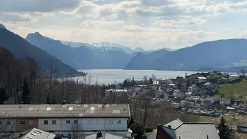 Panoramablick auf den See und die umliegende Berglandschaft mit einer Siedlung im Vordergrund.