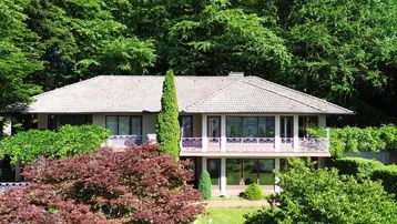 Elegante Villa mit mehreren Balkonen, umgeben von üppigem Grün und einem gepflegten Garten.