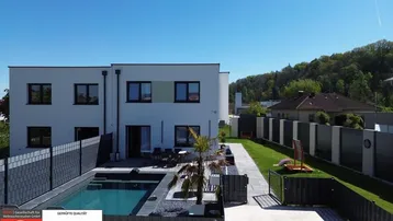 Modernes Haus mit Pool, Terrasse und Gartenbereich unter blauem Himmel.