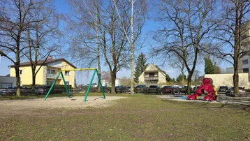 Sonniger Kinderspielplatz mit Schaukeln und Bäumen in der Wohnanlage.