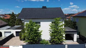 Frontansicht eines Einfamilienhauses mit Vorgarten und Carport unter blauem Himmel.
