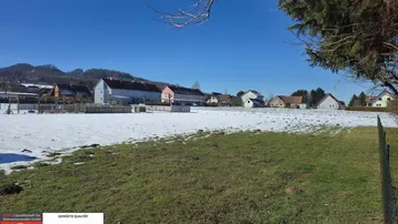 Weitläufiges Grundstück mit Schneeresten und Blick auf die umliegende Wohnbebauung und Hügellandschaft.