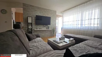 Gemütliches Wohnzimmer mit großem Sofa, modernem TV-Bereich und hellen Fenstern.