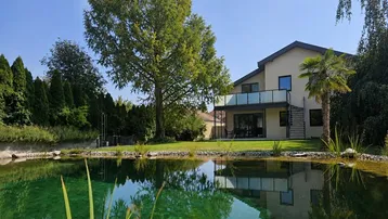 Großzügiger Gartenbereich mit einem natürlichen Teich und Blick auf das moderne Wohnhaus.