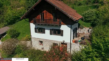 Traditionelles Haus mit Holzbalkon und Steinfassade, umgeben von üppiger grüner Natur.