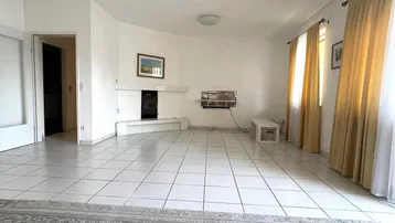 Geräumiges Wohnzimmer mit hellen Fliesen, Kamin und großen Fenstern mit gelben Vorhängen.