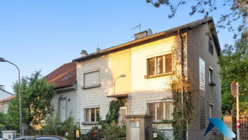 Fassade eines Mehrfamilienhauses mit hellen Steinplatten und grüner Bepflanzung.