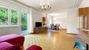 Geräumiger Wohn-Essbereich mit Parkettboden, Stuckdecke und Zugang zum Balkon.