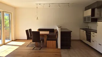 Heller offener Wohn-Essbereich mit Holzboden und Zugang zu einem Balkon oder einer Terrasse.