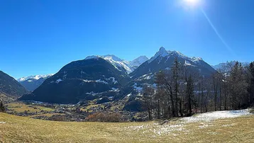 Weitläufiges Panorama der schneebedeckten Alpen und eines grünen Tals unter strahlend blauem Himmel.