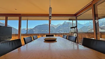 Heller Essbereich mit großem Holztisch und raumhohen Fenstern mit beeindruckendem Bergblick.