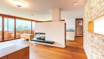 Heller Wohnbereich mit modernem Kamin, Holzboden und großen Fenstern mit Bergblick.