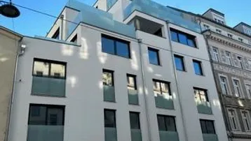 Moderne Fassade eines Wohngebäudes mit großen Fenstern und Balkonen in städtischer Umgebung.