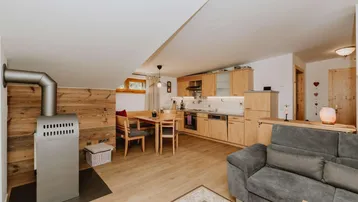 Offener Wohn-Essbereich mit integrierter Küche, Holzofen und gemütlicher Sitzecke.