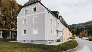 Mehrfamilienhaus mit heller Fassade und Satteldach in ländlicher Umgebung.