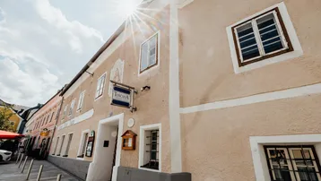 Historisches Gebäude mit traditioneller Fassade und Sonnenschein, das eine Pizzeria beherbergt.