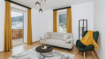 Helles Wohnzimmer mit modernem Sofa, Holzboden und Zugang zu einem Balkon mit Bergblick.