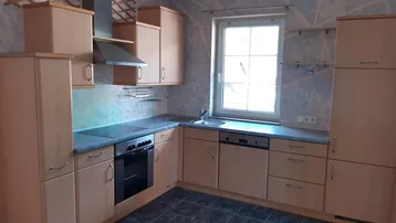 Funktionale Küche mit hellen Holzschränken, Einbaugeräten und einem Fenster über der Spüle.