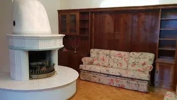 Gemütliches Wohnzimmer mit traditionellem Kachelofen, floralem Sofa und Holzeinbauten.