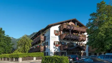 Traditionelles Gebäude mit Holzbalkonen und Bergblick in einer alpinen Umgebung, umgeben von Grünflächen.