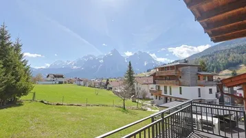 Weitläufiger Blick von einem Balkon auf die schneebedeckten Berge und grüne Wiesen.