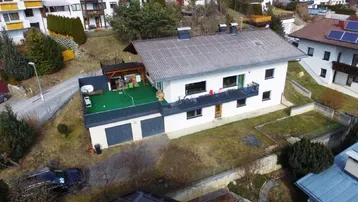 Luftaufnahme eines Hauses mit grüner Kunstrasenfläche auf der Terrasse und umliegenden Wohnhäusern.