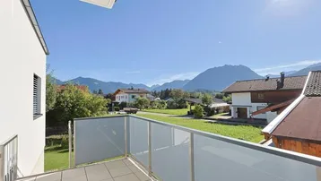 Heller Balkon mit Glasgeländer und weitem Blick auf die umliegende Berglandschaft.