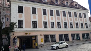 Historisches Gebäude mit mehreren Stockwerken und Dachgauben, an einer gepflasterten Straße gelegen.