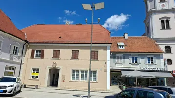 Historisches Gebäude mit Ziegeldach und braunen Fensterläden an einem sonnigen Tag auf einem Platz.