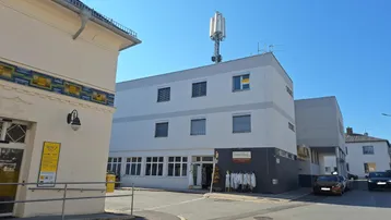Gebäudeansicht von der Straße mit einem Mobilfunkmast auf dem Dach unter blauem Himmel.