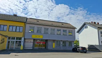 Gebäudeansicht von der Straße mit Postfiliale und angrenzendem Möbelgeschäft unter blauem Himmel.