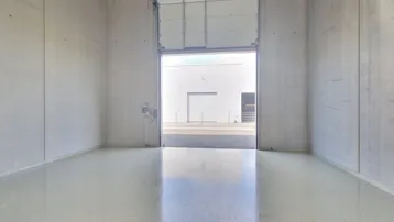 Geräumiger, leerer Industrieraum mit glänzendem Boden und offenem Rolltor, das viel Tageslicht hereinlässt.
