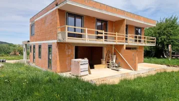 Neubau eines Einfamilienhauses im Rohbauzustand mit sichtbaren Ziegelwänden und provisorischem Balkongeländer.