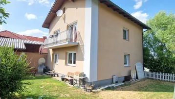 Einfamilienhaus mit beiger Fassade, Balkon und großem Gartenbereich.